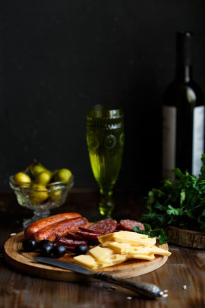Aperitif table Meat snack, fried sausages, cheese, salami, olives and a glass of wine on a dark table Menu and restaurant conceptの写真素材