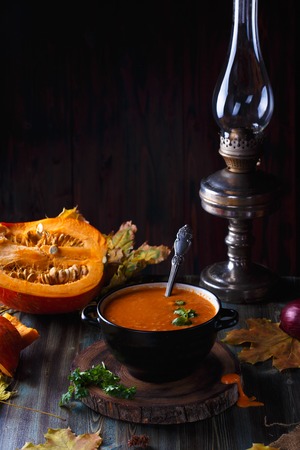 Pumpkin soup puree with greens in a plate on a dark table. On the background of pumpkinsの写真素材