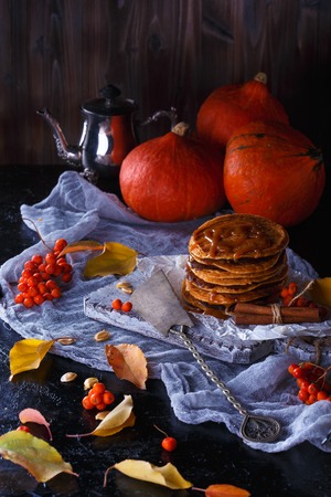 Autumn concept. Pumpkin pancakes with caramel topping, with pumpkins, leaves on a dark background.の写真素材