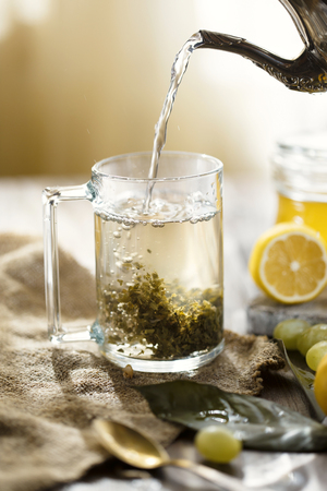 Pour tea from a teapot into a mug. On the table are lemons and grapes. Morning conceptの写真素材