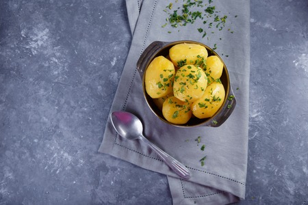 Hot boiled potatoes in a plate sprinkled with herbs with cutlery on a gray background Top view Copy spaceの写真素材