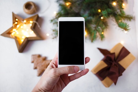 female hand with a phone takes pictures of New Year's decorations and fir branches. New Year and Christmas conceptの写真素材