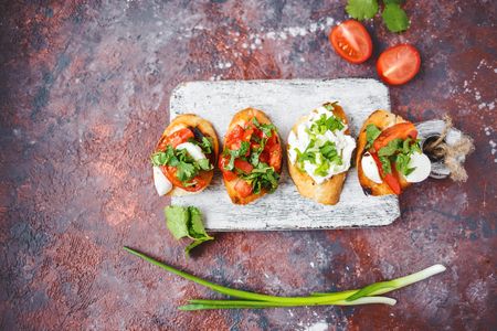 several types of italian bruschetta with tomatoes, mozzarella and herbs on a wooden board on a dark background Copy spaceの写真素材