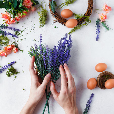 women's hands make an easter wreath of flowers, herbs and eggs on a light background. Easter concept Copy space Top viewの写真素材