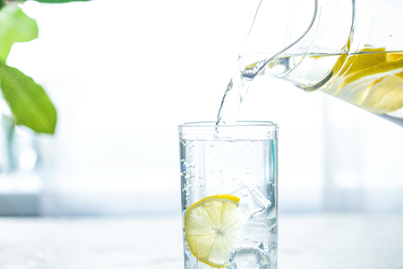 Pouring a glass of water with lemon, ice and mint on a white table Copy spaceの写真素材