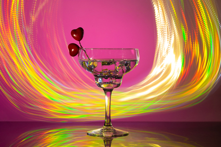 glass with a cocktail and two hearts. Valentine's day and wedding concept. On a dark pink background with freezelightの写真素材