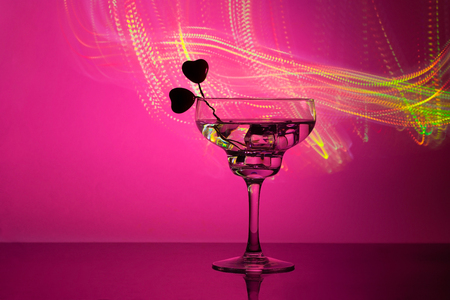 glass with a cocktail and two hearts. Valentine's day and wedding concept. On a dark pink background with light highlightsの写真素材