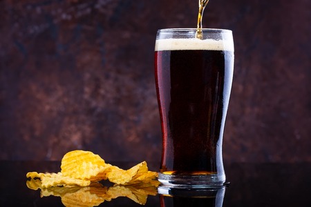 pouring beer into glass and chips on dark wooden background Copy spaceの写真素材