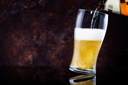 pouring beer into glass on dark wooden backgroundの写真素材