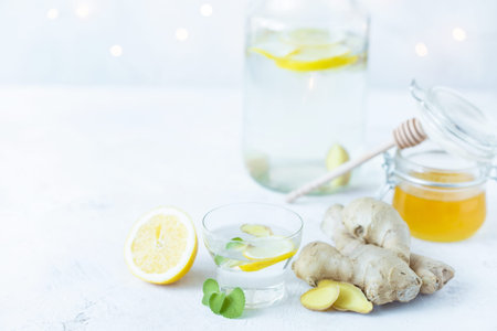 Healthy ginger drink in a cup. Ginger root, honey in a jar, lemon on a white table.