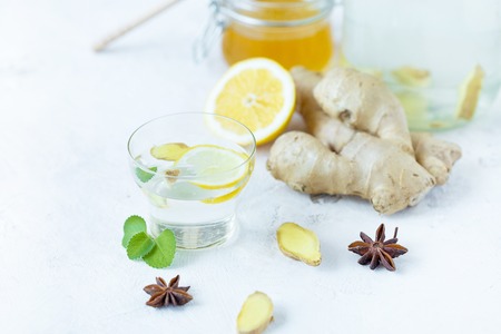 Healthy ginger drink in a cup. Ginger root, honey in a jar, lemon on a white table.の写真素材