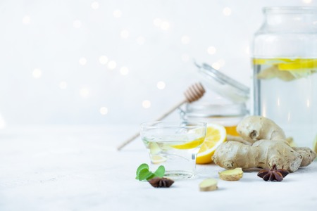 Healthy ginger drink in a cup. Ginger root, honey in a jar, lemon on a white table.の写真素材