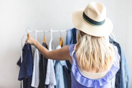Blondy girl in hat near a wardrobe with clothes can not choose what to wear. Concept has nothing to wear Choosing clothesの写真素材