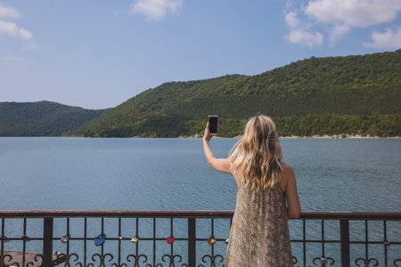 girl blogger traveler takes pictures on smartphone beautiful mountain lake and yachts
