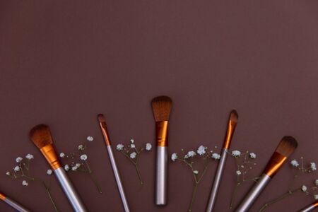 cosmetic makeup brushes with white flowers on a brown background Copy space Cosmetic beauty concept Top view Flat layの写真素材