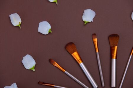 cosmetic makeup brushes with white pentals roses on a brown background Copy space Cosmetic beauty concept Top view Flat layの写真素材