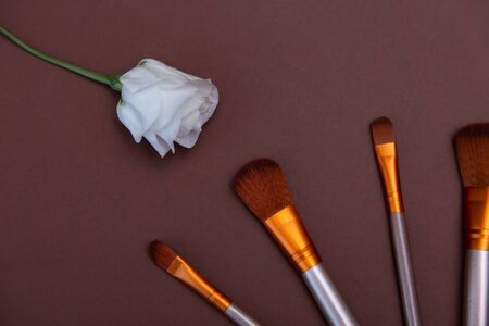 cosmetic makeup brushes with white roses on a brown background Copy space Cosmetic beauty concept Top view Flat layの写真素材