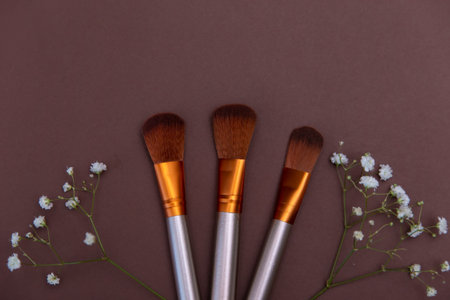 cosmetic makeup brushes with white flowers on a brown background Copy space Cosmetic beauty concept...
