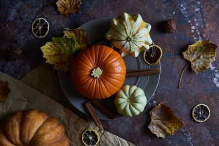 Pumpkin on a plate. Autumn cozy background with leaves, vanilla. Dark background Top viewの写真素材