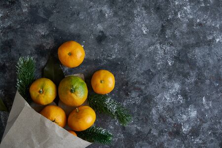 Tasty tangerines with leaves and fir branches in a paper bag on a dark background New Year Chrismas conceptの写真素材