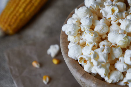 Traditional popcorn in a wooden bowl and corncobs on the table. Rustic country style