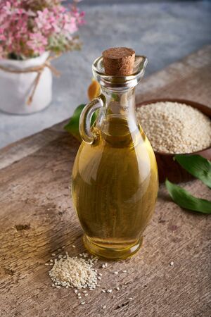 Sesame oil in glass bottle and sesame seeds on wooden background Verticalの写真素材