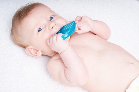 The baby s teeth are being cut. A cute kid with blue eyes nibbles a toy.