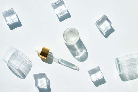 Cosmetic bottle of essence with a dropper and ice on a background of beautiful palm shadowsの写真素材