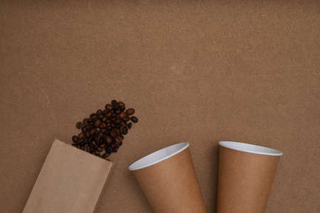 Two disposable craft glasses with package and coffee beans on craft background . Monochrome photo Copy spaceの写真素材