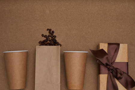 Two disposable craft glasses with package, gift box and coffee beans on craft background . Monochrome photo Copy spaceの写真素材