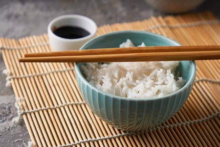 Rice in a porcelain bowl, with Japanese chopsticks, soy sauce, served on a gray stone table Copy...