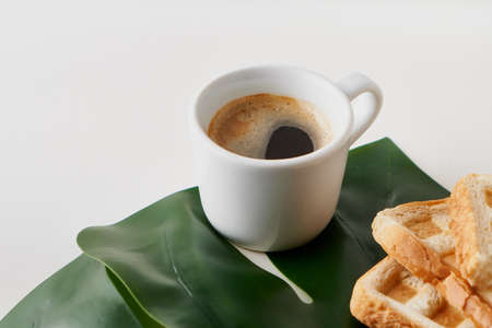 Morning coffee in white cup with fried toast and plant leaf on white table Copy spaceの写真素材