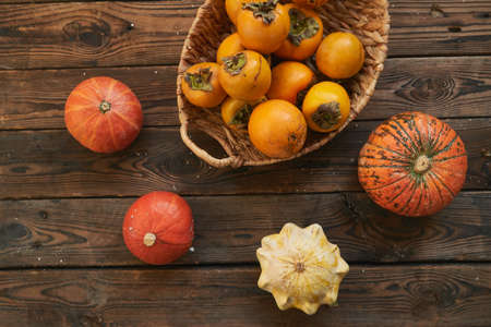 basket with a harvest of persimmons and pumpkins on a wooden table. Country style Food backgroundの写真素材