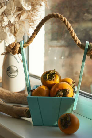 basket with a harvest of persimmons on the windowの写真素材