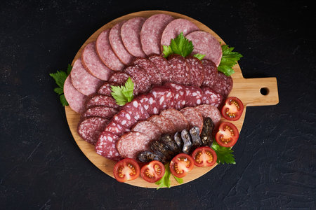 Assorted sliced sausages of different flavors. Served on a beautiful wooden tray, with herbs and...