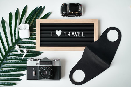 Travel flat lay. Camera, protective mask, headphones, board with inscription I love Travel on white...