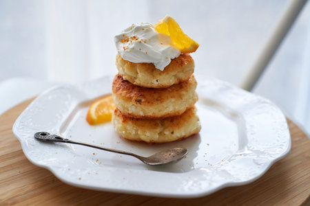 baked cottage cheese tortillas, sirniki with sour cream and orange peel served on white plate