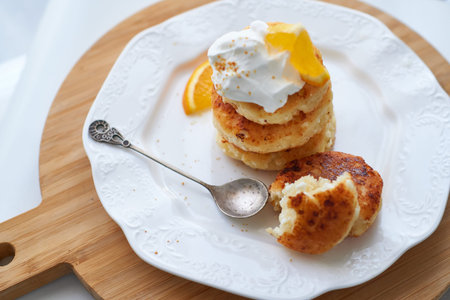 baked cottage cheese tortillas, sirniki with sour cream and orange peel served on white plate