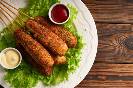 Tasty corn dog with sauce and salad served on white plate on wooden tableの写真素材