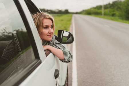 Happy young woman travels by car on the road.の写真素材