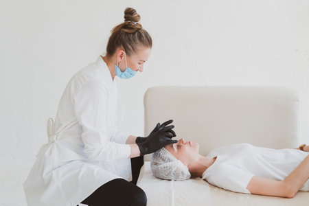 Beautician masseur doing facial massage to young womanの写真素材