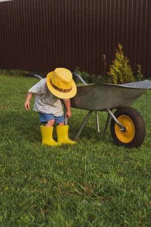 Cute two year old toddler in a straw hat playing in garden cart filled with sand