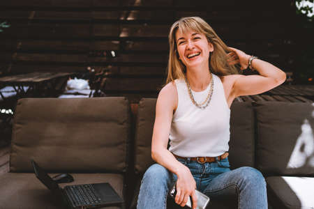 Portrait of a young beautiful woman sitting with a laptop and a phone on the sofa in a cozy work areaの写真素材