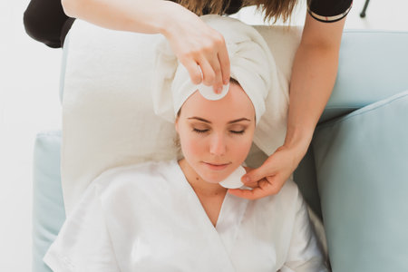 beautician makes facial and massage to adorable young woman with a towel on her headの写真素材