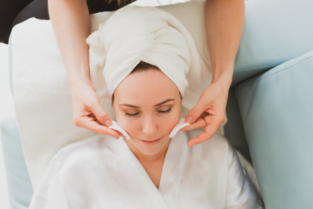 beautician makes facial and massage to adorable young woman with a towel on her headの写真素材