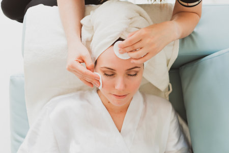 beautician makes facial and massage to adorable young woman with a towel on her headの写真素材