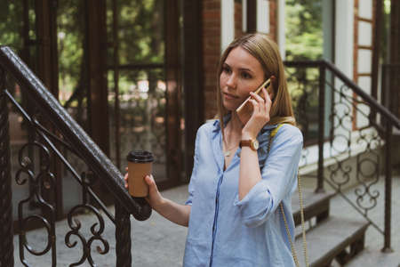 young charming woman with coffee in her hands talking on the phone on the city streetの写真素材