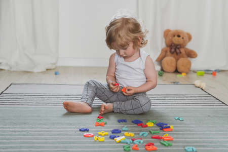 little cute toddler playing with toy letters sitting on the floorの写真素材