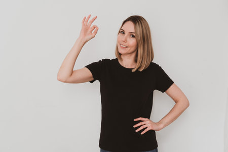 Portrait of young European woman in casual clothes pointing with finger ok sing. On white background. Hand gesturesの写真素材