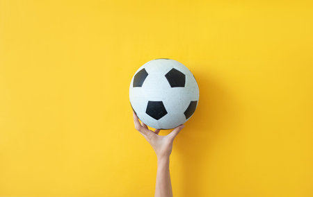 Female hand holding soccer ball on yellow background Concept photo